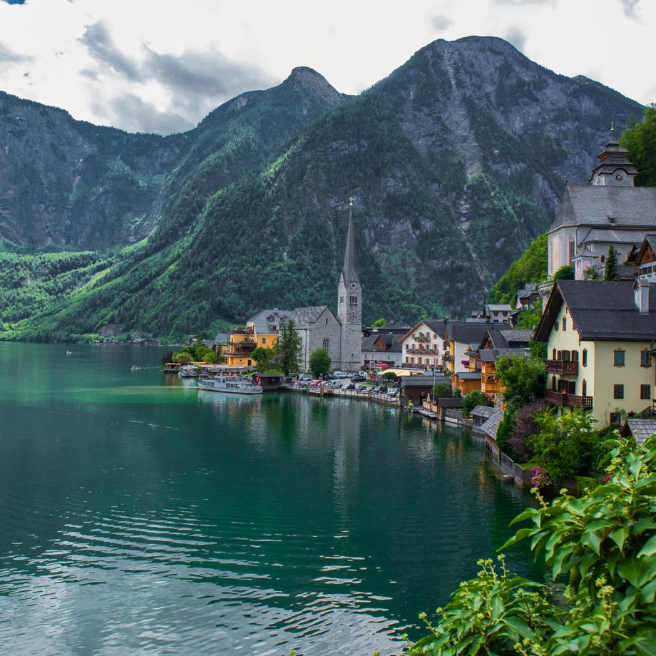 Picturesque view of Hallstatt with church and mountains reflecting on the calm lake waters.